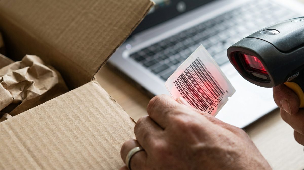 A small shop owner scanning a product barcode into a laptop next to an open cardboard delivery box