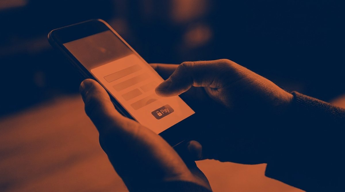 A close-up of a person entering card details on a smartphone at a UK online checkout, with a screen showing a Stripe payment form