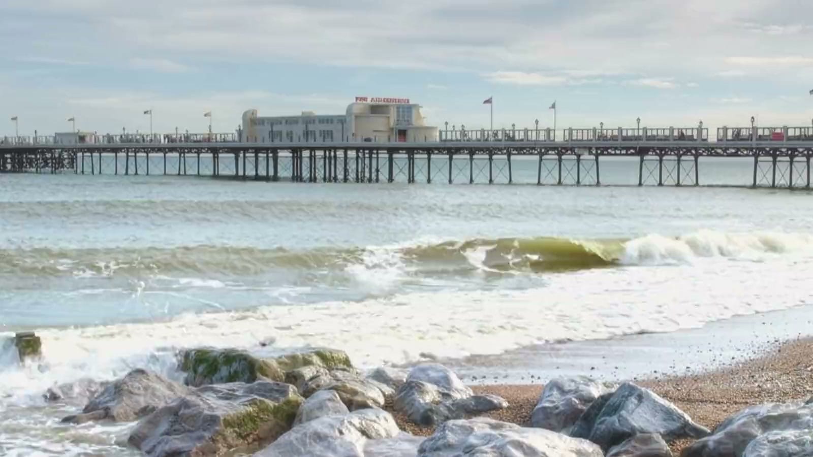 Worthing Pier seen from the shingle beach, with the sea washing over the boulder sea defences