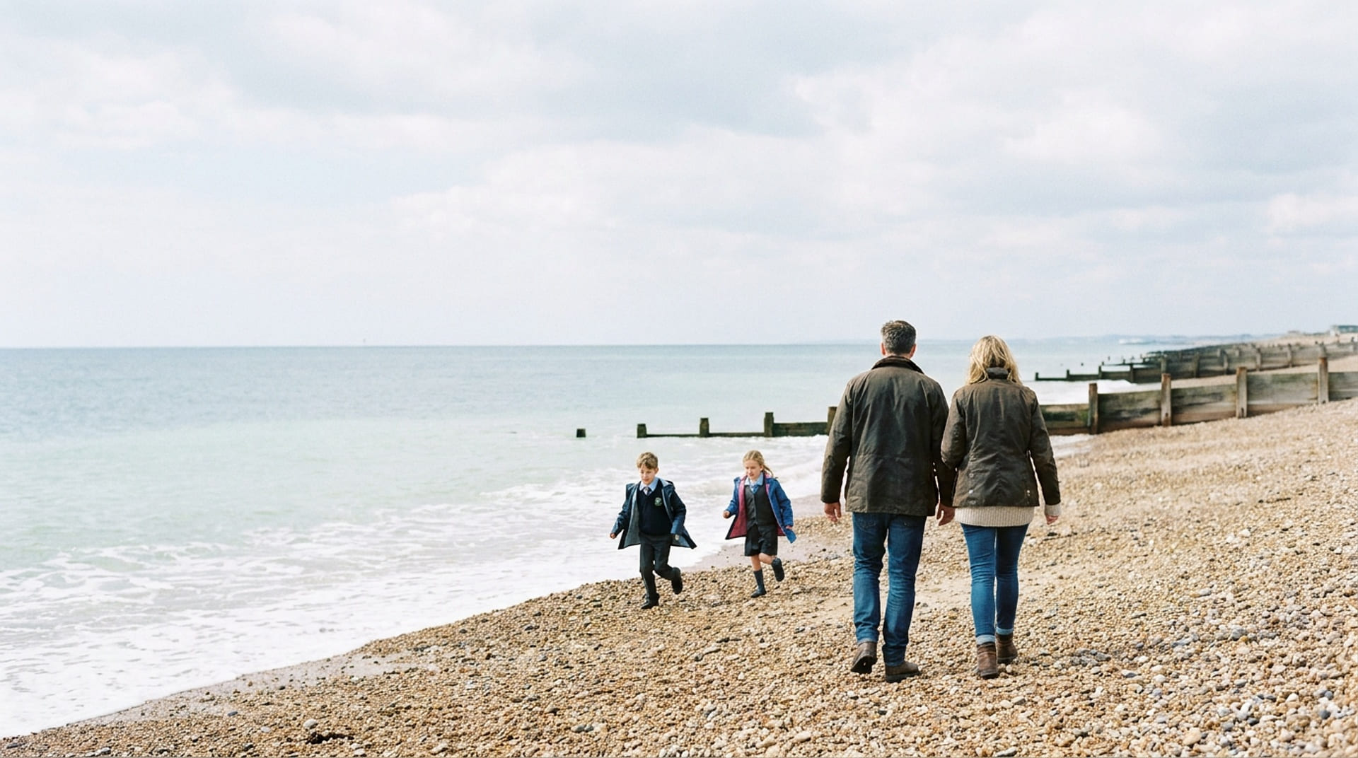 A family walking along a shingle beach past the timber groynes