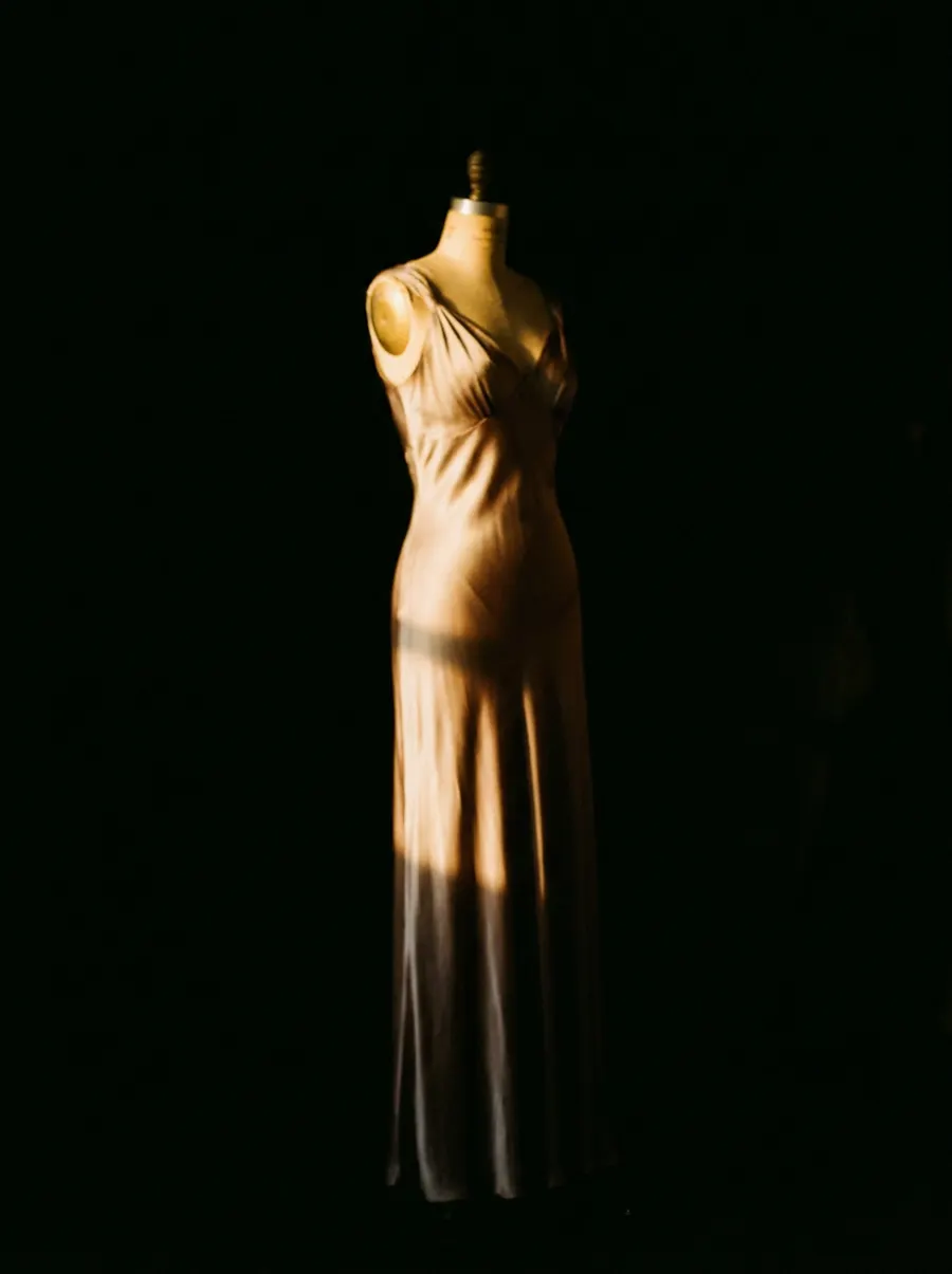 A silk evening gown on a dress form, lit from one side