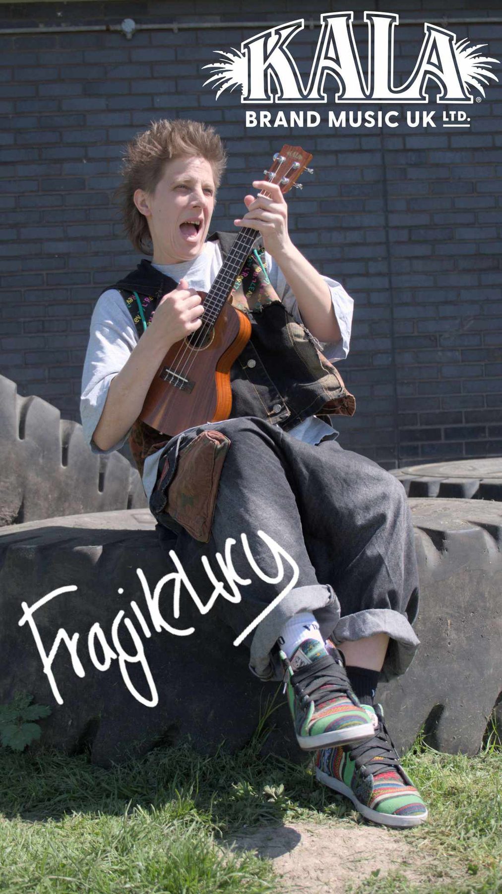 Fragile Lucy sitting on a tyre wall with her ukulele, Kala Brand Music UK