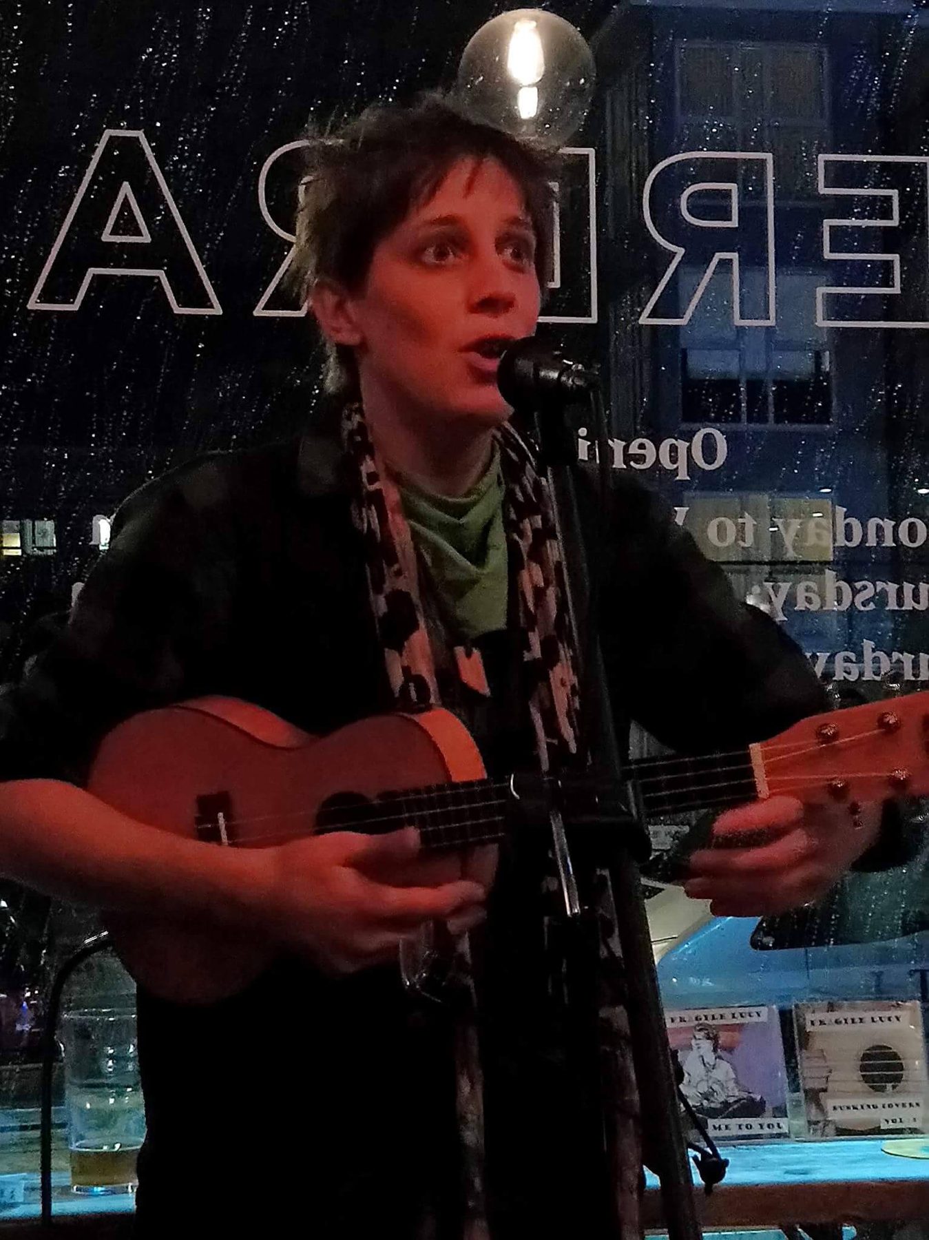 Fragile Lucy singing at a bar at night with her ukulele