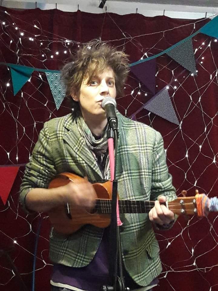 Fragile Lucy in a tweed jacket singing under bunting and fairy lights