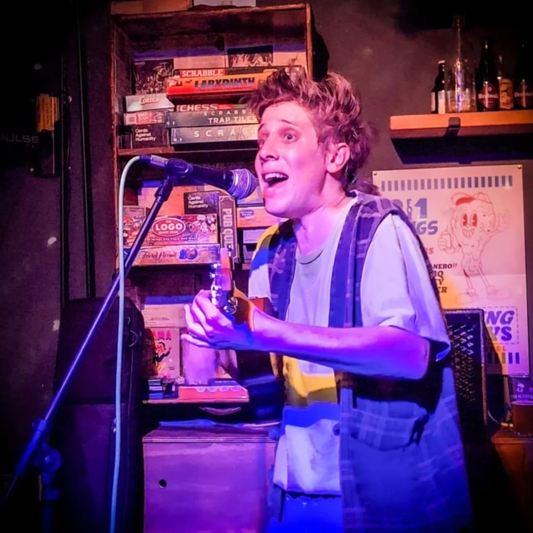Fragile Lucy grinning at the microphone under purple light