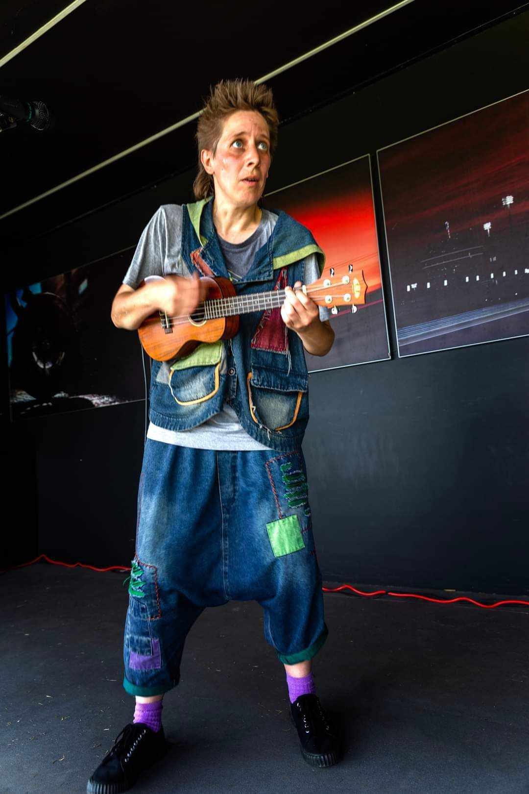 Fragile Lucy in patched denim playing ukulele on stage