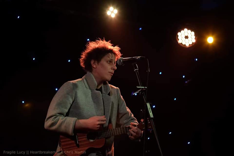 Fragile Lucy playing ukulele on a stage lit with tiny star lights