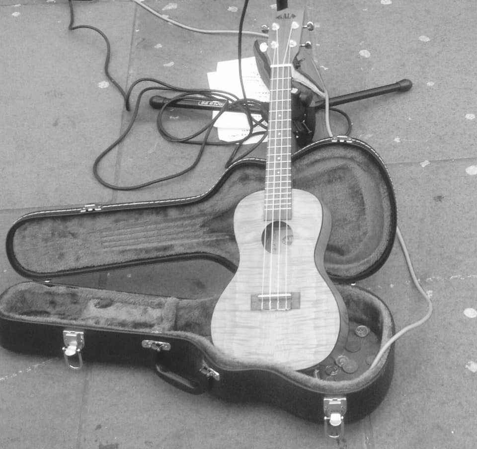 A ukulele resting in its open case on the pavement