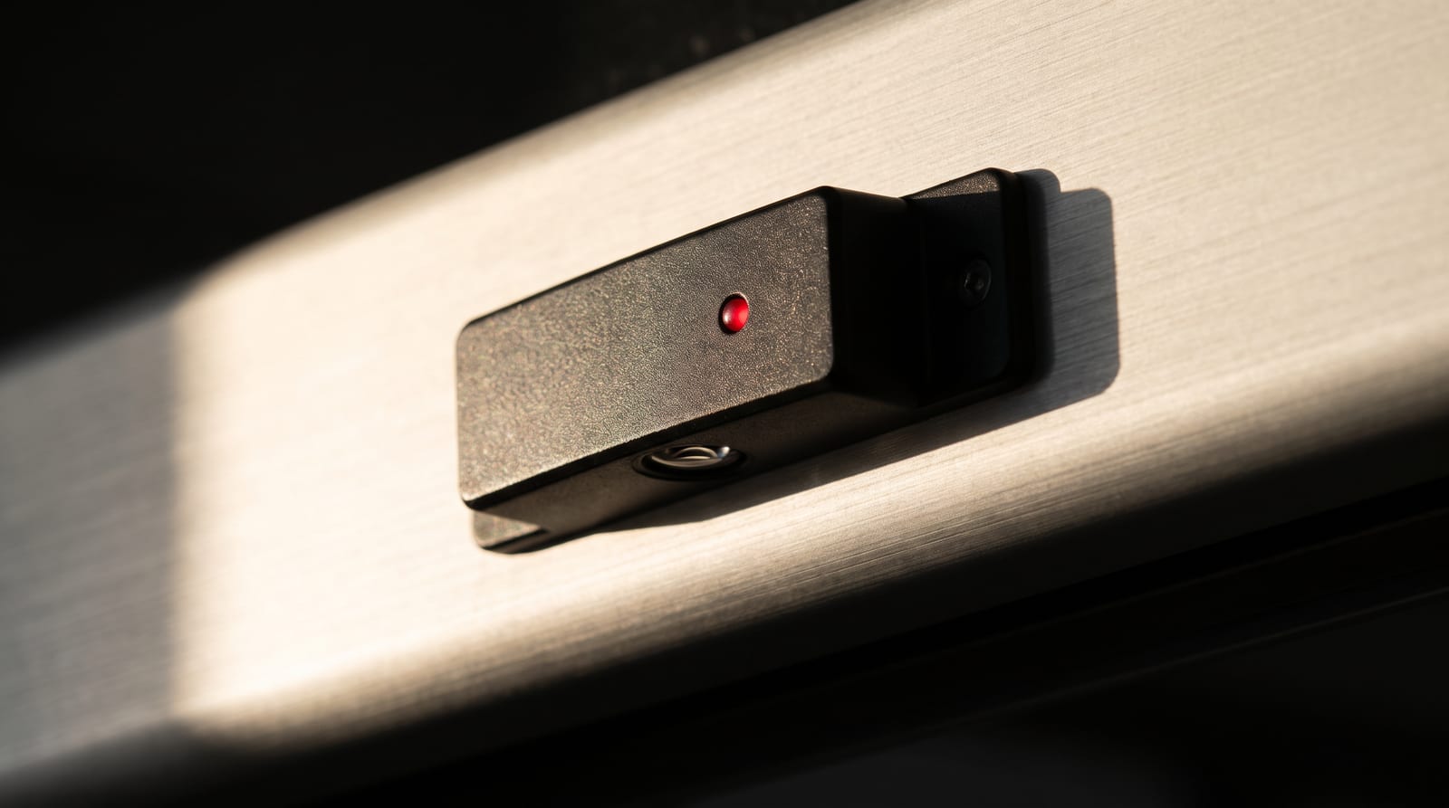 Close-up of an automatic door safety sensor on a brushed aluminium header, a small red status light lit