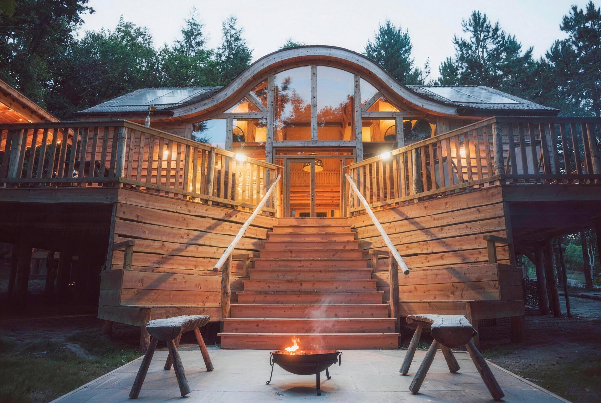The Journeyman cabin at dusk, with a curved roof, twin staircases and a lit fire pit